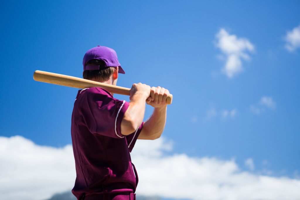 Low angle side view of baseball player holding bat against blue sky